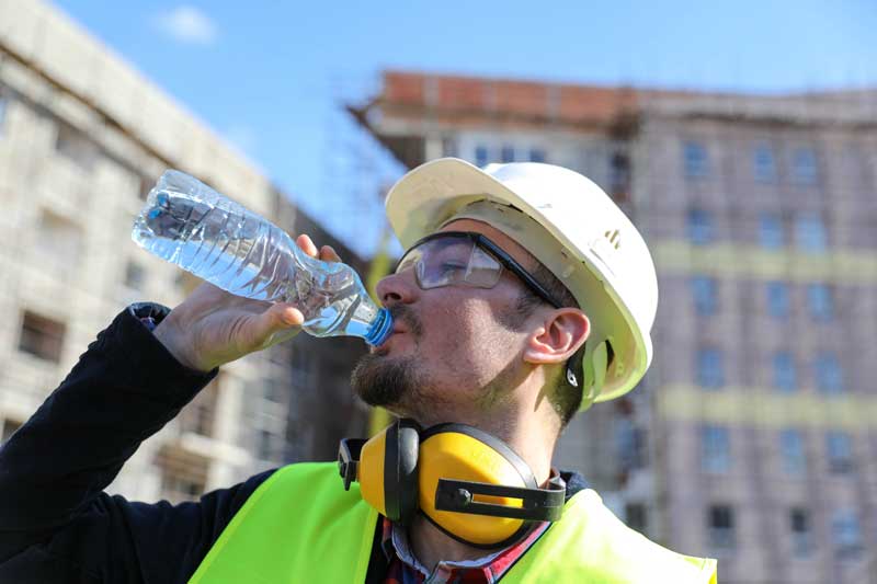 Empleado de la construcción hidratándose para no sufrir problemas de salud por trabajar con calor
