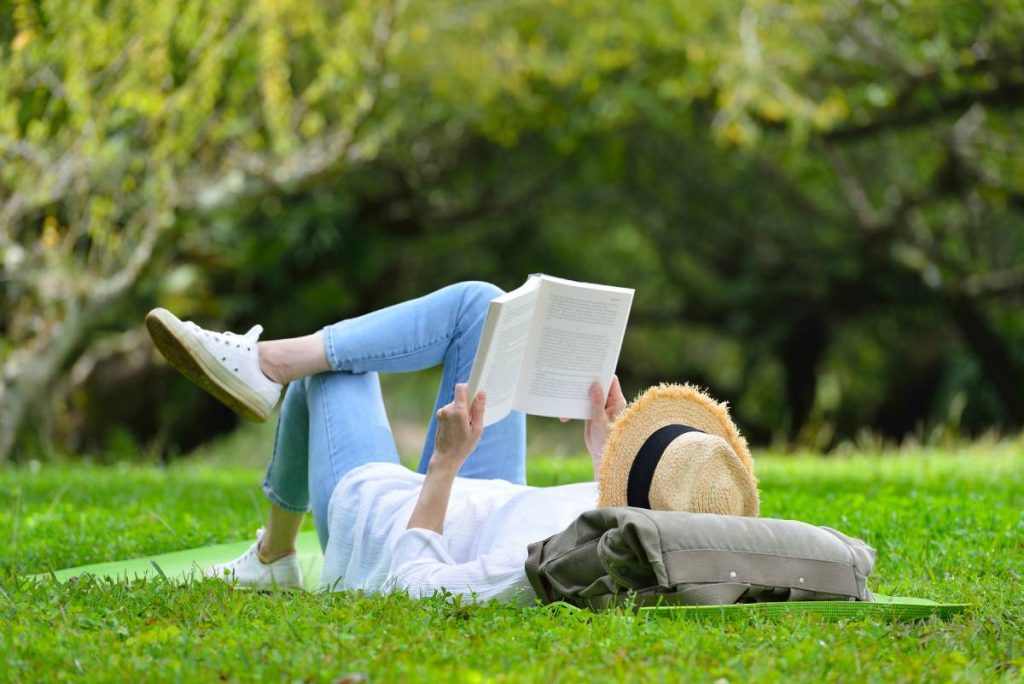 Mujer tumbada en la hierba leyendo un libro de RRHH en el parque